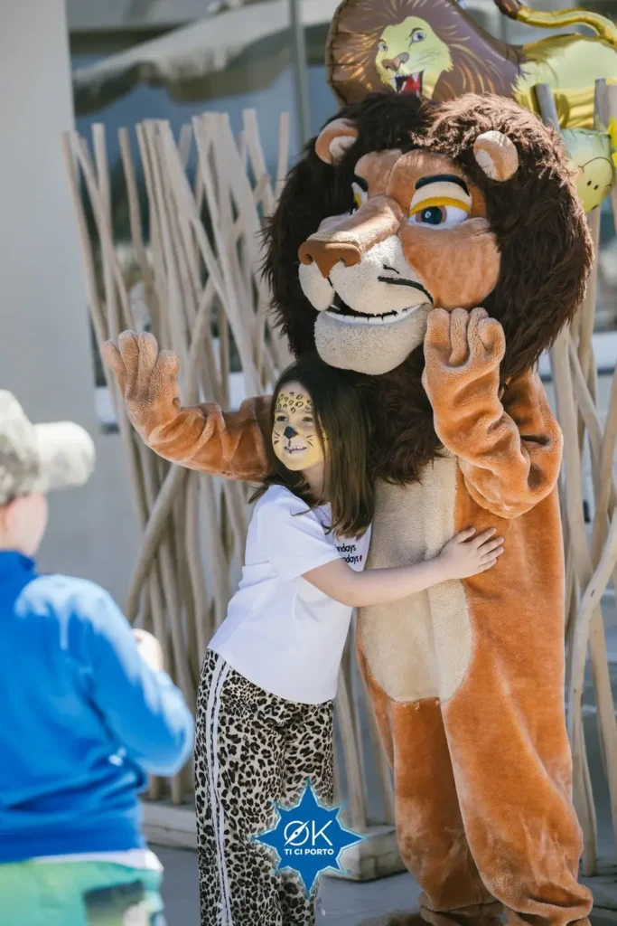 Bambina con trucco da leoncino abbraccia la mascotte leone allo spettacolo tributo di Ok ti ci porto