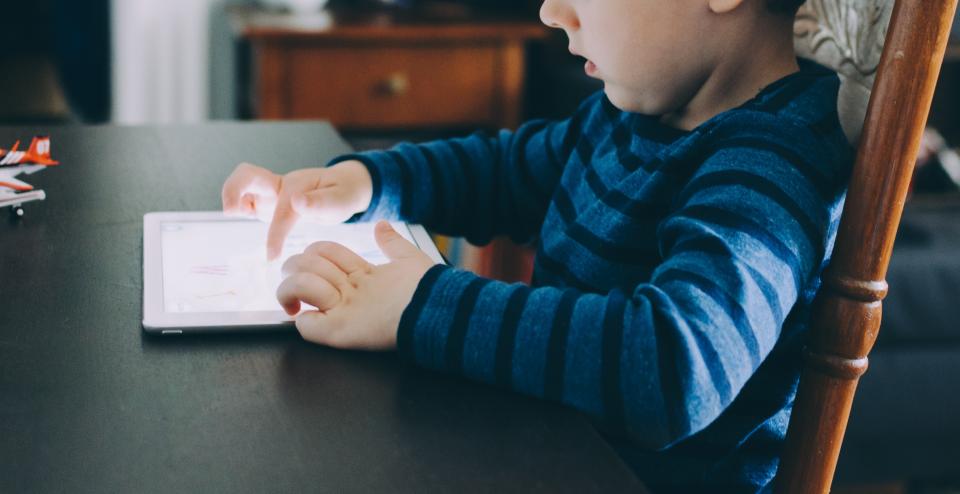 Bambino seduto sul divano che gioca con un tablet: infanzia e tecnologia