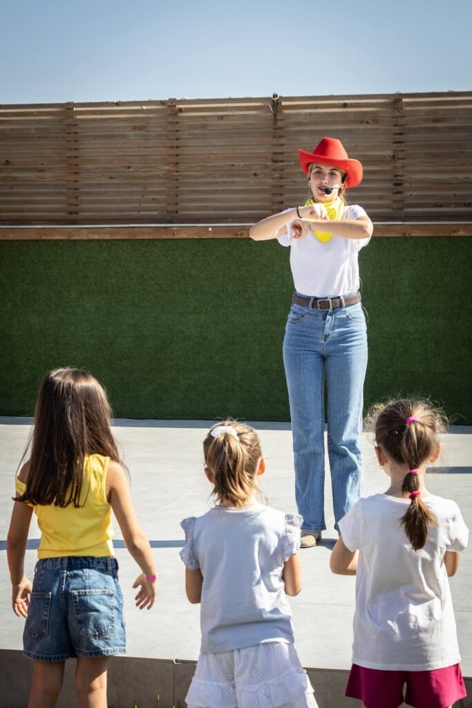 Un'animatrice con il cappello rosso e il microfono davanti ad alcune bambine che la guardano