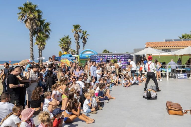 Il pubblico seduto sul pavimento davanti al palco, con un artista in camicia bianca e bretelle rosse